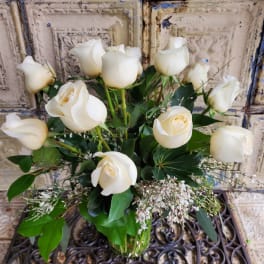 White roses arranged in a clear glass vase with greenery