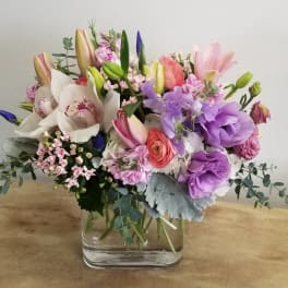 Mixed bouquet of lilies, orchids, and purple blooms in a glass vase