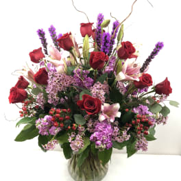 Red roses and pink lilies in a glass vase with purple filler flowers