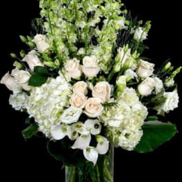 White floral arrangement with roses, hydrangeas, and calla lilies in a glass vase