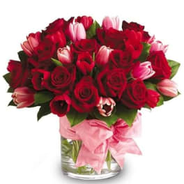 Red roses and pink tulips in a glass vase with a pink ribbon