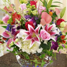 Mixed bouquet of pink lilies, roses, and orchids in a glass bowl vase