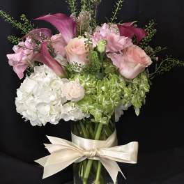 Pink calla lilies and roses in a glass vase with a cream ribbon