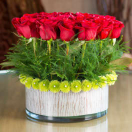 Red roses arranged in a low glass vase with green accents
