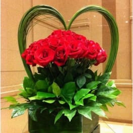 Red roses arranged in a heart-shaped basket with green foliage