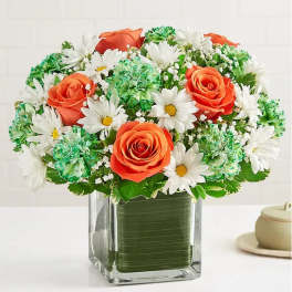 Orange roses and white daisies in a clear square vase