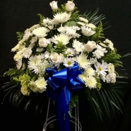 White floral standing spray with a blue ribbon on a metal easel