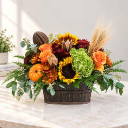 Autumn floral arrangement with sunflowers, roses, mums, and pumpkins in a wooden basket