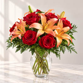 Red roses and peach lilies arranged in a clear glass vase