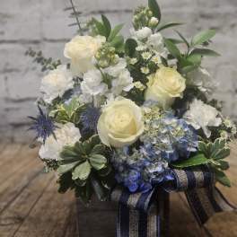 Cream roses and blue hydrangeas in a wooden box with a ribbon.