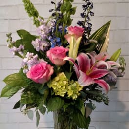 Pink roses and lilies in a clear glass vase with mixed purple blooms