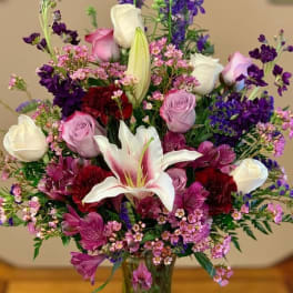 Mixed bouquet of lilies, roses, and purple flowers in a glass vase