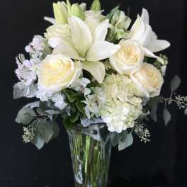 White lilies and cream roses arranged in a clear glass vase