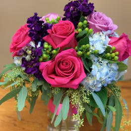 Bouquet of pink roses, purple blooms, and blue hydrangeas in a glass vase