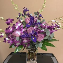 Purple orchids and pink roses arranged in a clear glass vase