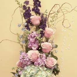 Tall floral arrangement with pink roses, hydrangea, and purple blooms in a silver vase