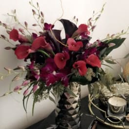 Tall bouquet of red calla lilies and purple orchids in a patterned vase