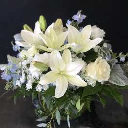 White lilies and roses arranged with pale blue flowers in a vase