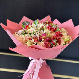 Pink-wrapped bouquet of peach roses and mixed lilies