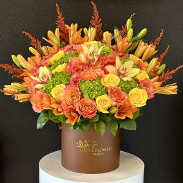 Orange and yellow floral arrangement in a brown hat box