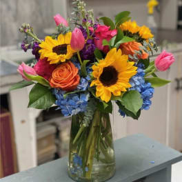 Colorful bouquet of sunflowers, roses, tulips, and hydrangeas in a glass vase