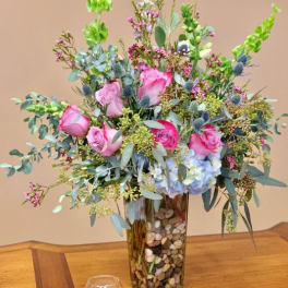 Pink roses and blue hydrangea in a tall glass vase with pebbles