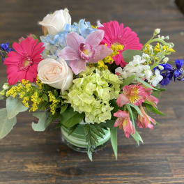 Mixed bouquet in a striped vase with pink daisies, roses, hydrangea, and orchids
