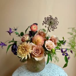 Peach and cream bouquet in a ribbed glass vase with purple accents