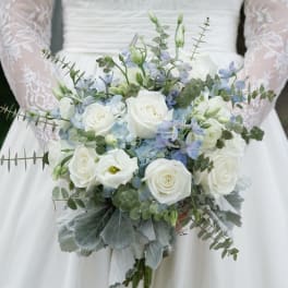 Bride holding a white and pale blue bouquet with roses and greenery