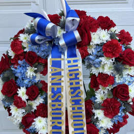 Heart-shaped floral wreath with red, white, and blue flowers and a ribbon