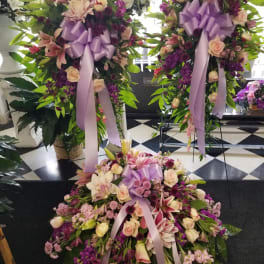 Three large floral standing sprays with lavender ribbons and mixed pink-purple blooms