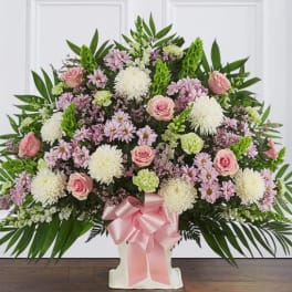 Large pink and white floral arrangement in a white vase with a pink ribbon