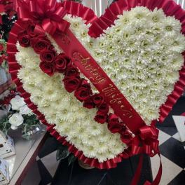 Heart-shaped floral arrangement with white daisies and red roses, wrapped in red ribbon.
