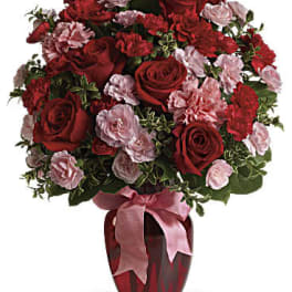 Red roses and pink carnations in a red vase with a pink ribbon