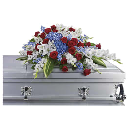 Casket spray with red roses, white lilies, and blue flowers