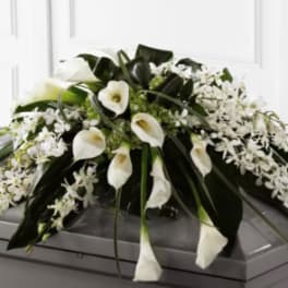 White calla lilies and orchids arranged on a gray casket