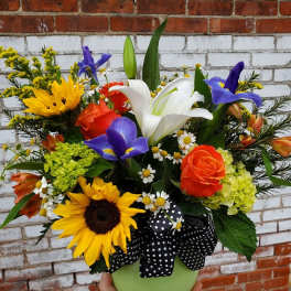 Mixed bouquet with lilies, roses, sunflowers, and irises in a green vase