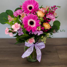 Pink gerbera and mixed flowers in a glass vase with a lavender ribbon