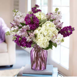 Purple and white flowers arranged in a purple glass vase