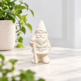 Small ceramic gnome figurine on a tabletop beside a potted plant
