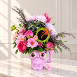Pink and purple flowers arranged in a purple skull vase with a spider decoration