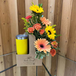 Mixed bouquet with sunflowers, roses, and gerbera daisies in a gift box beside a yellow tumbler
