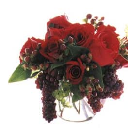 Red rose bouquet with dark berry accents in a clear vase