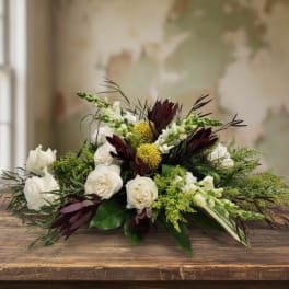 Low centerpiece of white roses, green accents, and dark burgundy blooms in an elongated design