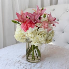 Pink lilies and roses arranged with white hydrangeas in a glass vase.
