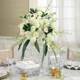 White floral centerpiece in a tall clear vase on a set table