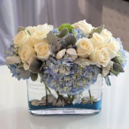 Cream roses and blue hydrangeas arranged in a clear glass vase