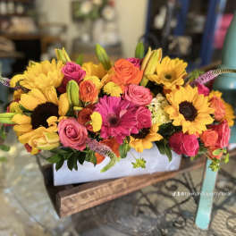 Bright mixed bouquet with sunflowers, roses, and lilies in a white container