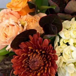 Close-up of peach roses, rust chrysanthemum, and white hydrangeas in a clustered arrangement