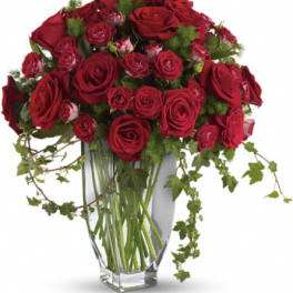 Red roses arranged in a clear glass vase with trailing ivy